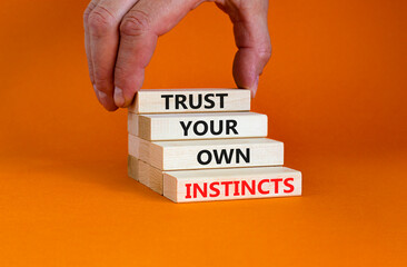 Trust your own instincts symbol. Wooden blocks with words 'Trust your own instincts'. Beautiful orange background. Businessman hand. Copy space. Business and trust your own instincts concept.