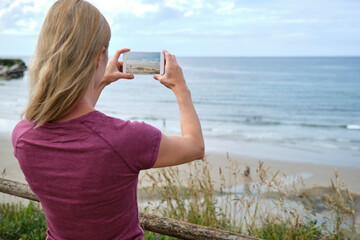 Rear view of a traveling girl taking a photo from the beach boardwalk.