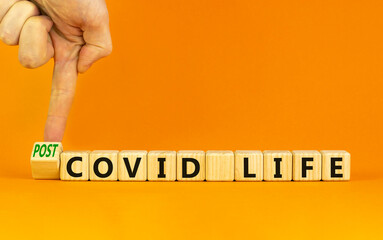 Symbol for a post-covid life. Businessman turns a cube and changes words 'covid life' to 'post-covid life'. Beautiful orange background. Medical, business and covid-19 pandemic concept, copy space.