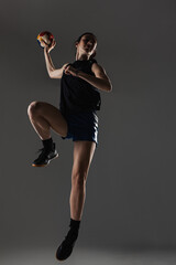 Handball player posing on gray background. Girl jumping with ball.