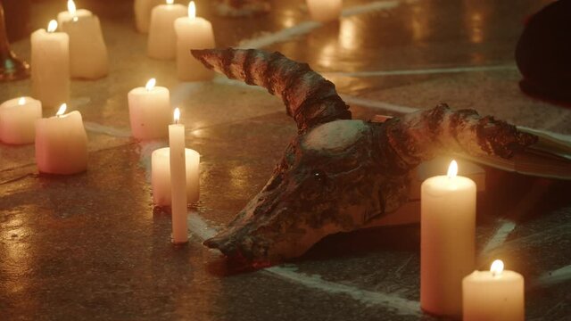 Cow skull and candles on floor close-up. Witch woman sitting in pentagram circle and reading spell. Evil sorceress making rite and sacrifices at night, using black witchcraft. Halloween time.