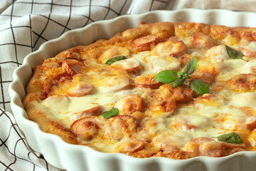 pizza with sausages, basil and cheese in a white dish