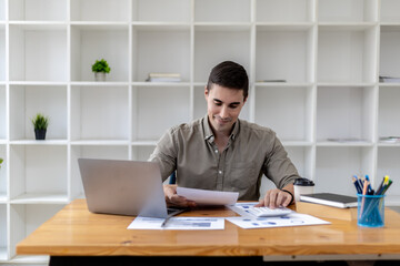 Fototapeta na wymiar Young businessman sitting and checking financial documents displayed in chart format, young businessman who founded a startup company, managing a new business to grow by leaps and bounds.