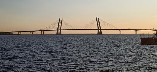 Cable-stayed bridge against the background of sunset. Ripples on the surface of the water. Western...
