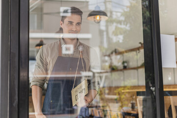 Fototapeta na wymiar Handsome man holding a sign in front of a shop, a café employee standing holding a sign saying open-close, he's flipping a sign saying 