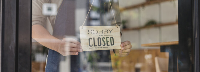Close-up shot of a closed sign in front of a storefront, a café employee standing holding a store...