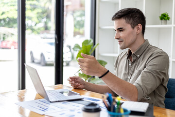 A young businessman is discussing a laptop video conference with a business partner who founded a startup company together, they have a company finance meeting to fix and plan financial arrangements.