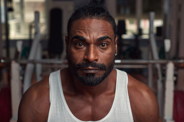 portrait of an attractive sports man Afro, who stands in the gym in a white T-shirt and looks directly into the camera. High quality photo