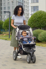 A young black mother walks with her child, who is sitting in a stroller