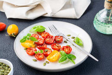 Diet vegetarian snack. Sun-dried tomatoes with basil, sesame seeds and pumpkin on a plate on a black background