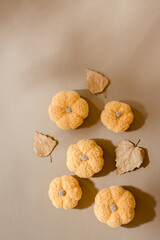 Handmade autumn still life of knitted pumpkins and dry birch leaves in the shade of a tree on cardboard. Pastel shades. Calm and warm mood. Vertical view