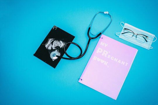 Stethoscope, glasses, medical mask, ultrasound picture of a child and pregnant book on a light blue background. Flat-lay, top view with place for your text. Medical trends and concept.