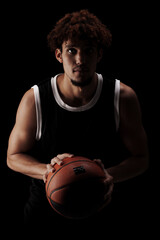 Professional basketball player holding a ball against black background. Serious concentrated...