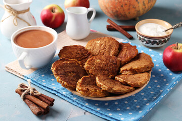 Pancakes with pumpkin and apples for breakfast, as well as a cup of coffee with milk on a light blue background.