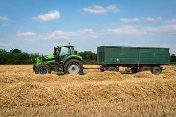 Obraz premium Getreideernte - am Feldrand wartet ein Schlepper mit Transportanhänger auf die Entladung des Mähdreschers.