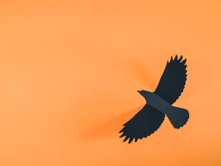 Black paper crow on an orange background.