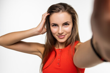 Fototapeta premium Beautiful young woman is making selfie with smartphone on white background