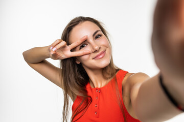 Obraz premium Portrait of a happy young woman making funny face while taking pictures of herself over white background