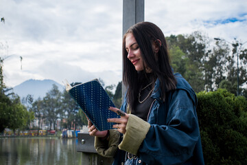 Young caucasian woman dressed in blue reading a book next to the lake in a green park