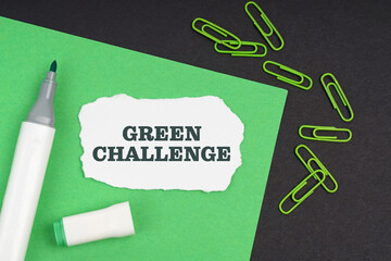 On a black background, a marker, paper clips, a sheet and torn paper with the inscription - Green challenge