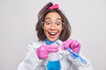Positive young Asian woman chemist mixes reagents conducts chemical experiment looks gladfully...