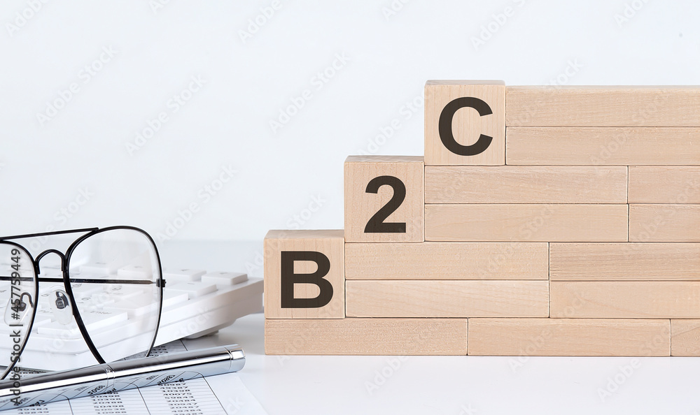 Poster three wooden cubes with letters b2c on the white table with keyboard and glasses