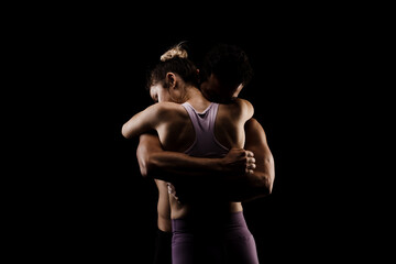 Fototapeta na wymiar Fit couple in love hugging together. Boy and girl side lit on black background.