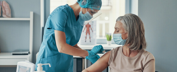 Young female nurse making vaccination to mature woman while working in the hospital