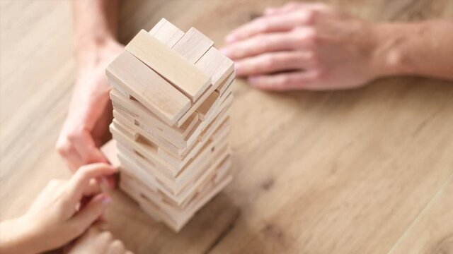 4k. Father and son playing wooden block removal tower game at home together. Board game Jenga. Kids leisure concept.