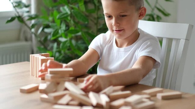 4k. Boy playing wooden block removal tower game at home. Board game Jenga. Kids leisure concept.