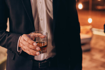 Close-up fo man in black suit holding glass with whiskey