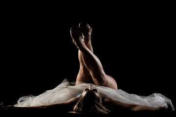 ballerina with a white dress and black top posing on black background. side lit silhouette.