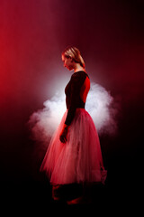ballerina with a white dress and black top posing on red smoke background © Nikola Spasenoski