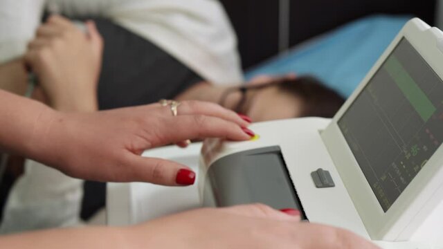 Pregnant Woman On Hospital Couch During Medical Control Cardiotocography. Gynecologist Doctor Hands Turn On Adjust CTG Device Clinic Consultant. Examine Expectant Belly Baby Mother Healthcare Check Up