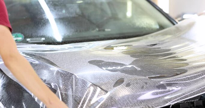 Man repairman wrapping protective vinyl film over car 4k movie