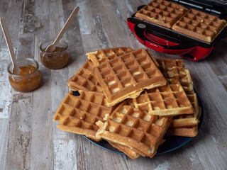 Belgian waffles stacked on top of each other and on a plate. Jam in a glass jar