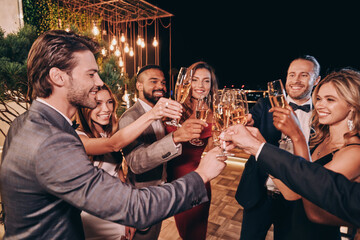 Group of beautiful people in formalwear toasting with champagne and smiling while spending time on luxury party