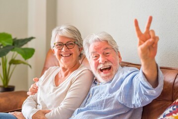 Portrait of cheerful senior couple embracing while sitting on sofa and laughing. Elderly happy...