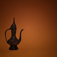 Vintage traditional islamic oriental engraved pitcher handmade on dark orange background. Elegant arabian antique tall metal jug.