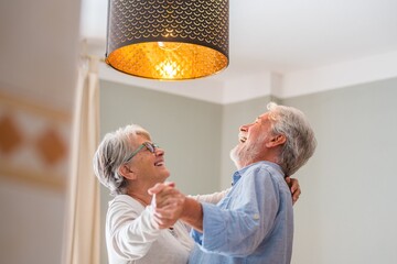 Cheerful senior couple dancing and laughing at home. Elderly happy couple celebrating by dancing in...