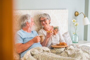 Old senior caucasian couple laughing and enjoying breakfast in the morning at bed in the bedroom at...