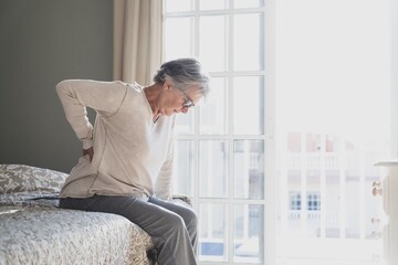 Tired senior woman suffering from backache after sleep, rubbing stiff muscles, Old female sitting...