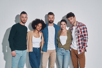 Obraz premium Group of young beautiful people in casual clothing bonding and smiling while standing against gray background