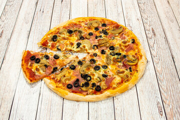 Small thin crust pizza with slices of black olives, slices of mushroom, cooked ham, oregano and a portion stretching the melted mozzarella cheese