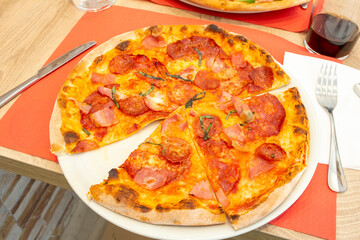 delicious Italian super thin crust pizza with smoked bacon and sliced spicy pepperoni on a plate at a restaurant table