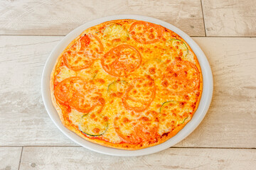 Pizza with slices of tomato and zucchini with lots of melted cheese on a white plate
