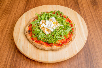 Small wheat flour dough pizza with arugula, tomato and cream cheese on top on wooden plate