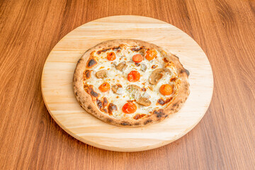 Small pizza with whole roasted cherry tomatoes, mushroom slices and lots of melted cheese with oregano on wooden plate