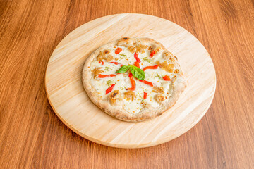 Small pizza with lots of melted mozzarella cheese, strips of roasted oregano red peppers and confit onion on round board