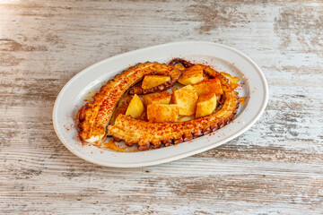 Stone roasted octopus tentacle with potatoes cooked with paprika, olive oil and sea salt on a white tray